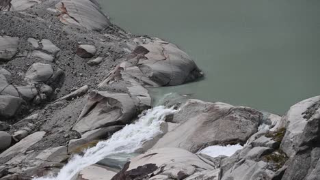 the rhone leaves a small lake and flows in the rocks, top of the alps, wallis, switzerland
