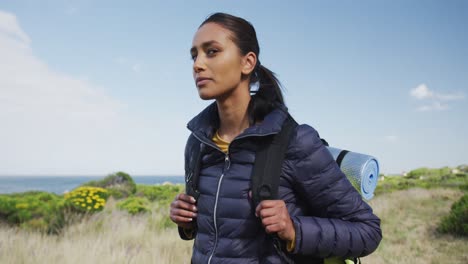 mujer de raza mixta con mochila mirando la cámara de senderismo en el campo