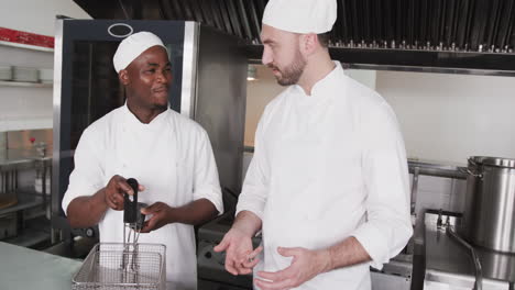 focused diverse male chef instructing trainee male chef in kitchen, slow motion