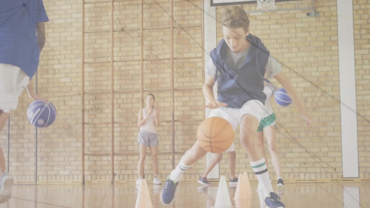 Studenti che sentono il segnale dell'allenatore e palleggiano con i palloni da basket per un esercizio zigzagando tra i coni arancioni