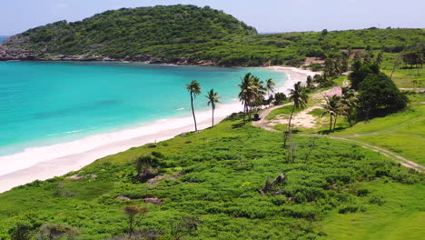 The-tropical-paradise-of-the-Half-moon-bay-beach-on-the-island-of-Antigua-enclosing-the-turquoise-blue-caribbean-sea-on-a-sunny-summer-day,-waves-washing-the-white-beaches,-aerial-scenic-view-4K