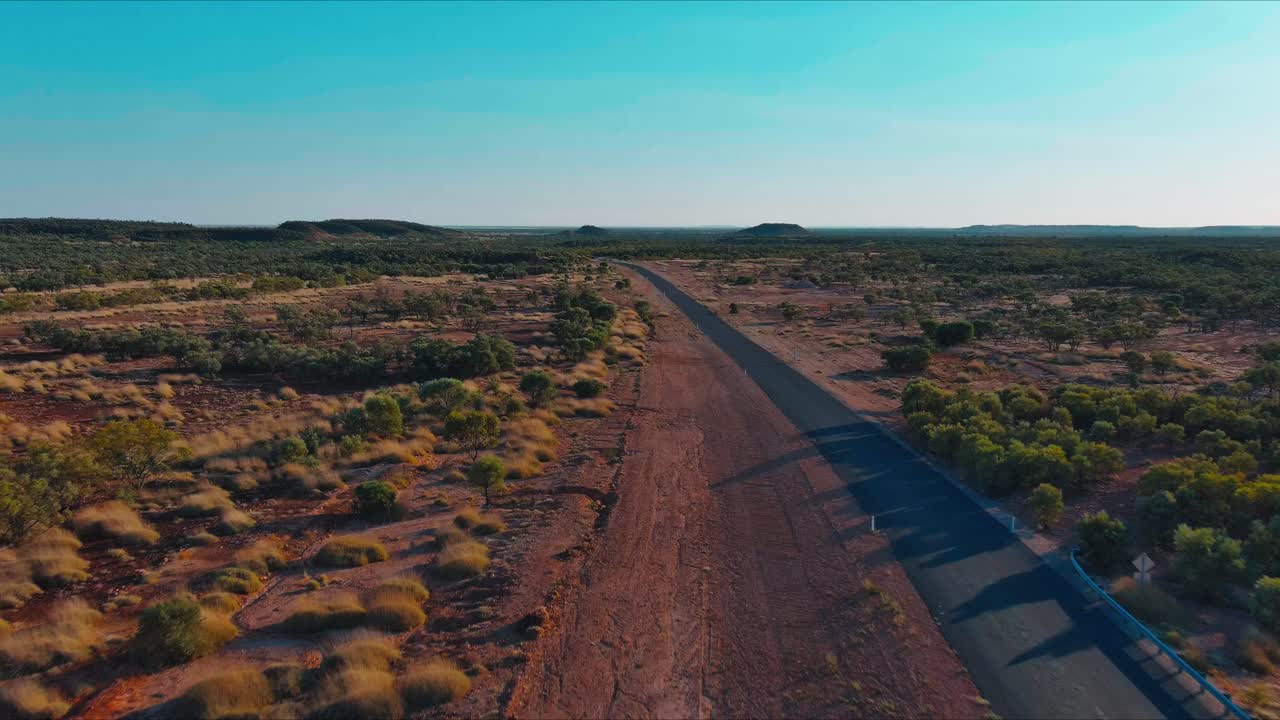 Vista aerea di un lungo tratto di strada statale in una remota cittadina dell'entroterra del Queensland, circondata da terreni accidentati e terra rossa polverosa