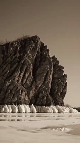 massive rock formation by a frozen lake in sepia tone