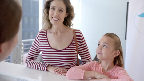 happy diverse girl patient mother and female nurse talking at hospital reception desk, slow motion