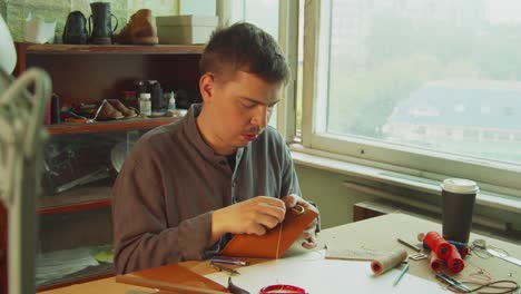 an old-school exclusive tailor makes handmade products from genuine leather in the workshop with thread and needle