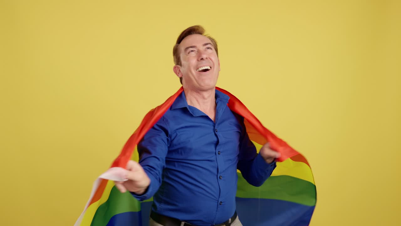 Happy Man Wrapped in Rainbow Flag Against Yellow Background