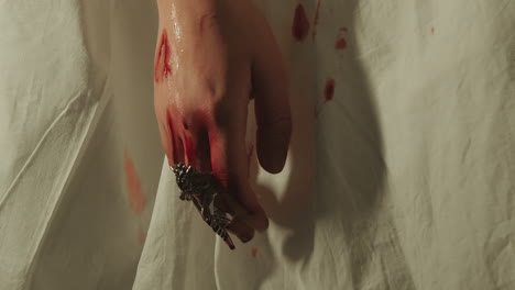 bloody hand with a large decorative ring and blood dripping onto a white sheet