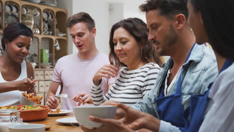 grupo de hombres y mujeres sentados alrededor de una mesa comiendo la comida que han preparado en la clase de cocina