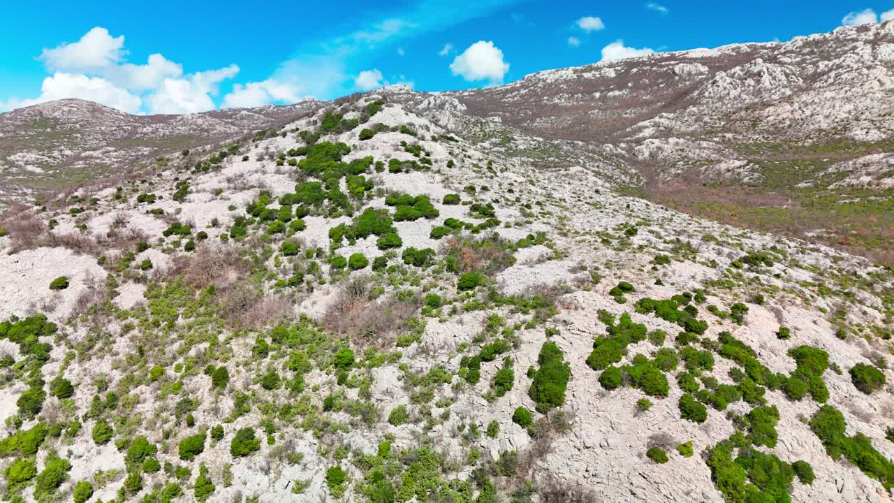 Drone trækker sig tilbage nær en Velebit-top i Zadar Amt, der viser klippeskråninger, sparsomme buske og det enorme bjerglandskab, der åbner sig i klart solskin.