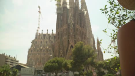 stunning video of a young caucasian female in a green dress with a knitted hat, observing incredible landmark building - sagrada familia, barcelona