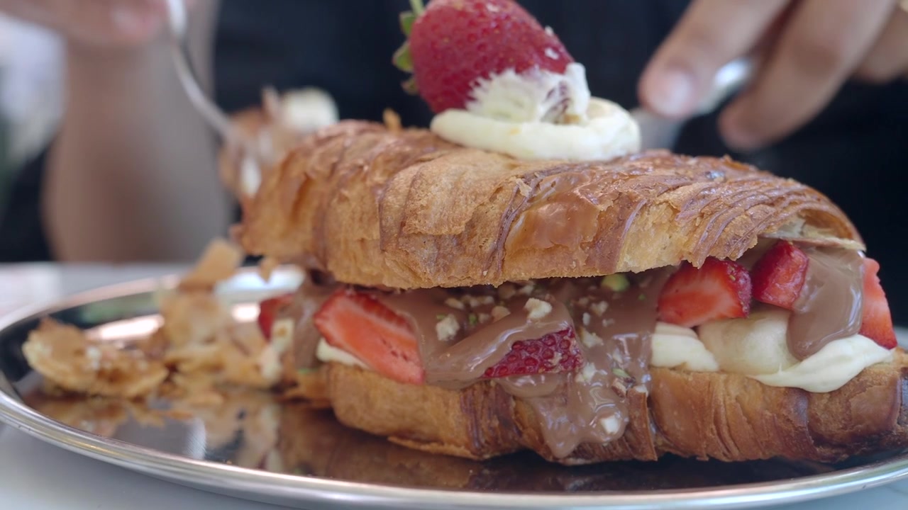 Persona che taglia un croissant gourmet alla fragola e cioccolato.