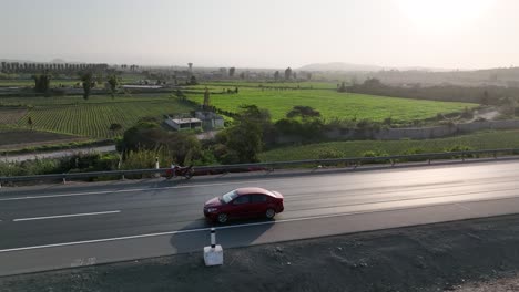 Drohne-Fliegt-über-Ein-Fahrendes-Auto-Entlang-Der-Autobahn,-Vorbei-An-Feldern-In-Der-Peruanischen-Landschaft,-Seitenansicht