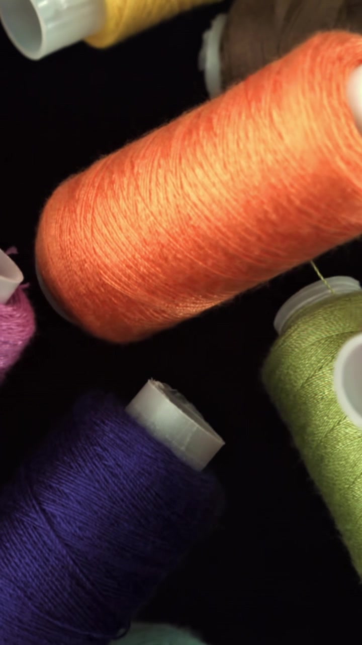 Close-up of Colorful Sewing Thread Spools Unwinding on Black Background