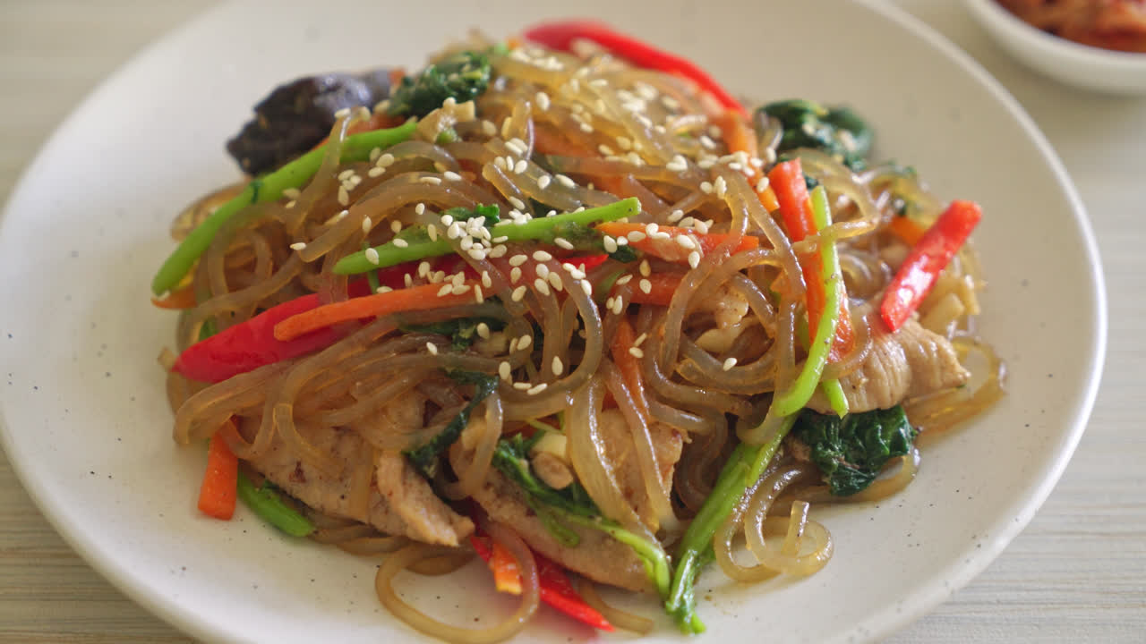 japchae o fideos vermicelli coreanos salteados con verduras y cerdo cubiertos con sésamo blanco - estilo de comida tradicional coreana