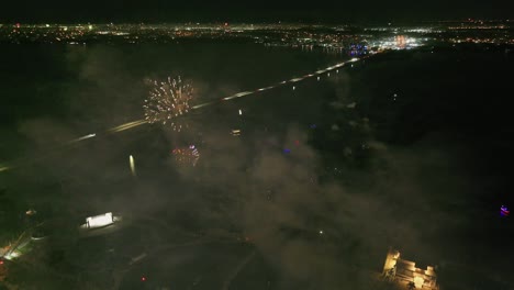 drone flight over glowing fireworks at dark night sky and illuminated city of fort myers, florida - top down view