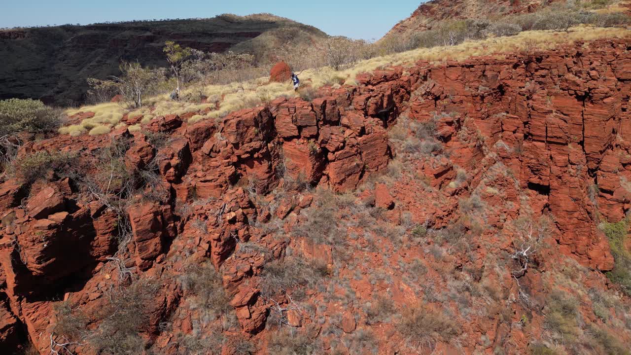 toma aérea de un hombre caminando a lo largo del borde de las montañas rojas australianas en verano - cámara lenta