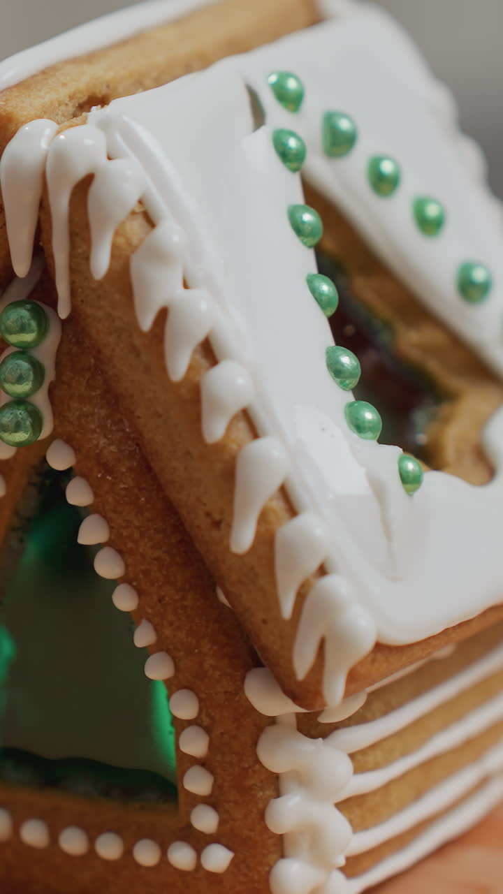 primer plano de manos que ponen helado en el techo de una casa de pan de jengibre, añadiendo detalles decorativos intrincados, estructura de galletas recién horneadas con perlas de azúcar verde en una bandeja de madera