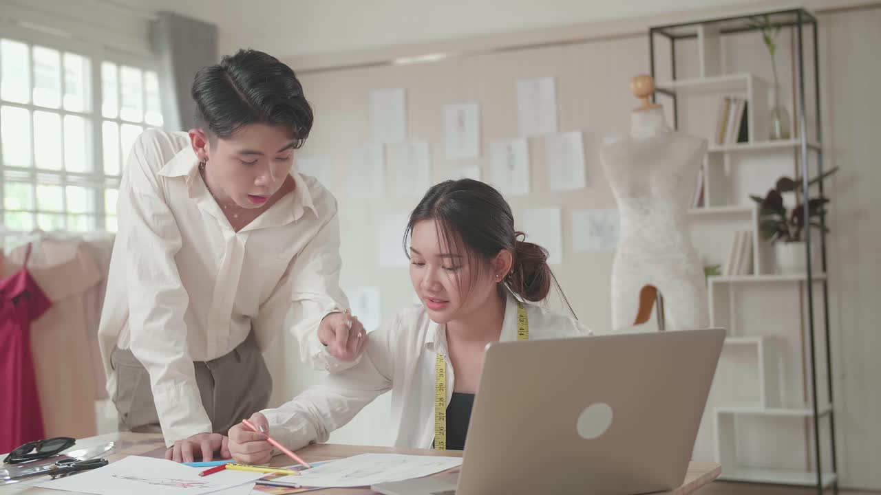 Two Young Asian Fashion Designers Working With Laptop And Sketching At Fashion Design Studio