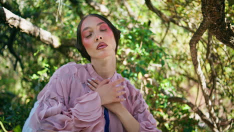 niña ninfa sentada en la naturaleza bajo las ramas verdes de los árboles de cerca. mujer hipnotizante