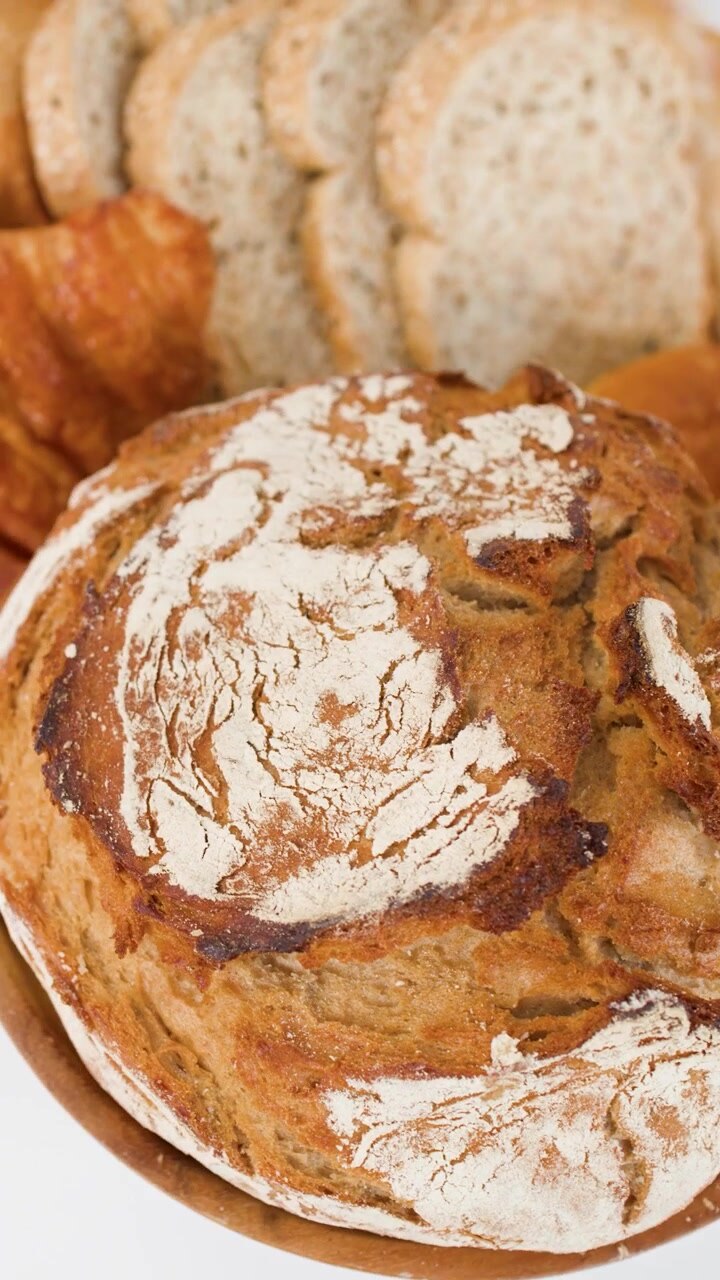 Close-up rotating view of crusty sourdough bread, croissants, and sliced whole wheat loaves.
