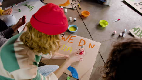 young environmental activists painting placards sitting on the floor