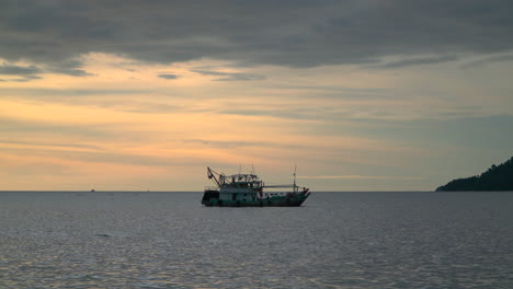 un barco pesquero anclado en el mar con puesta de sol en el fondo