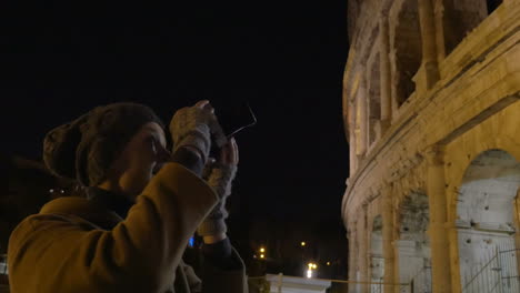 woman with retro camera shooting coliseum at night