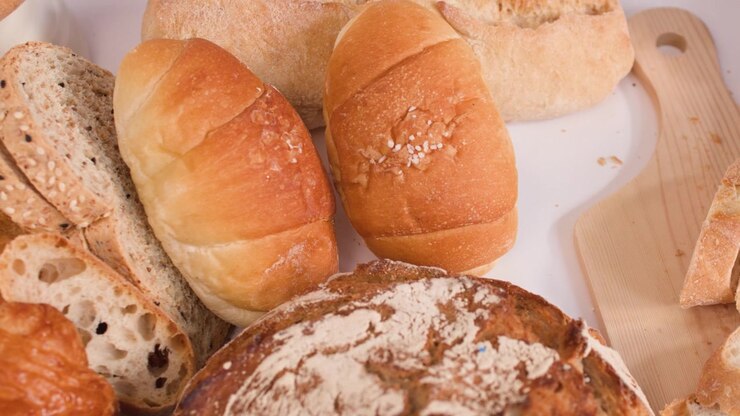 Close-up of hands slicing crusty bread on a wooden board amidst various artisanal loaves.