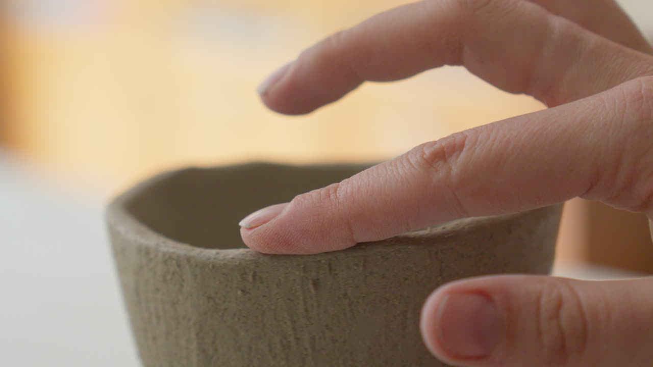 Dexterous fingers sculpt a clay cup's delicate form, close-up glimpse into an artisan's magical creation