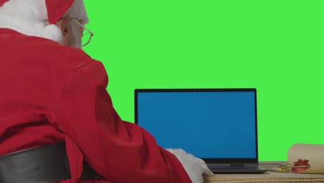 por encima del hombro de papá noel usando una computadora portátil con pantalla azul