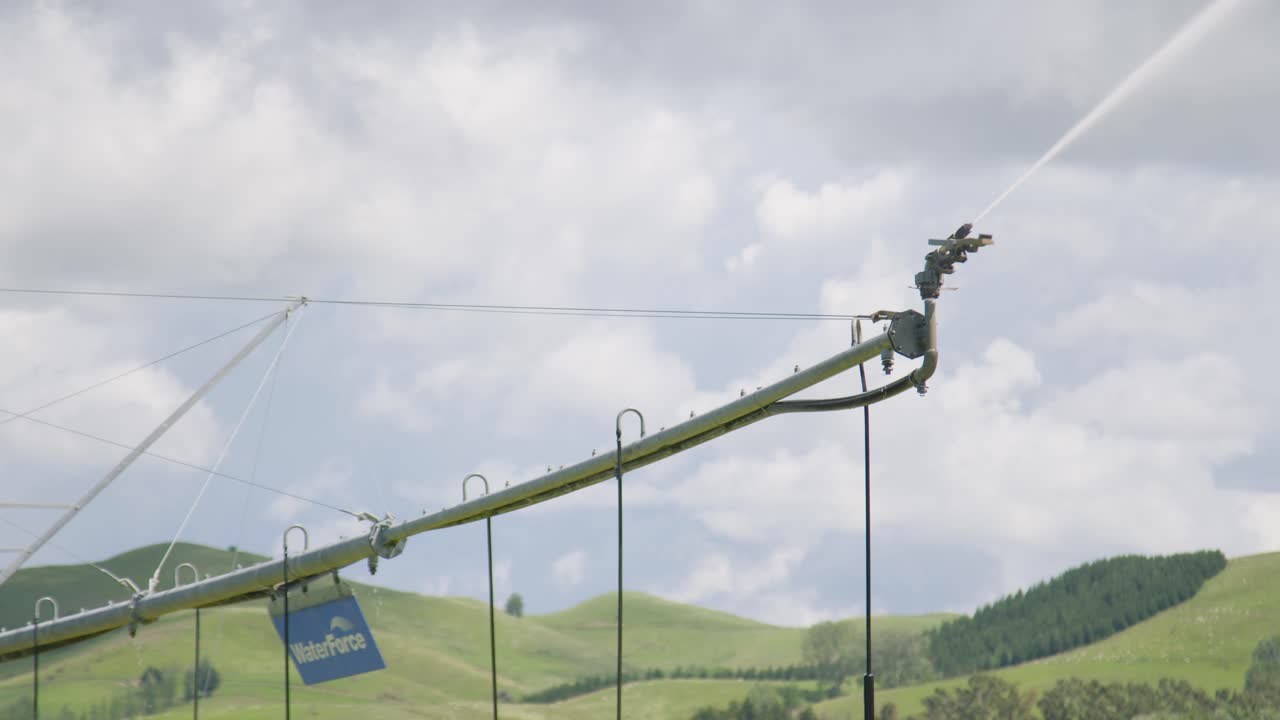 The water sprayer on the end of an irrigation truss, slowly moving with green rolling hills in the background