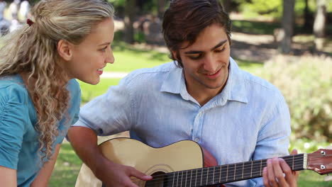 a boyfriend plays guitar for his girlfriend as they look at each other