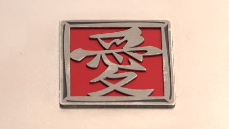 a red and silver square with asian characters lies on a pink surface