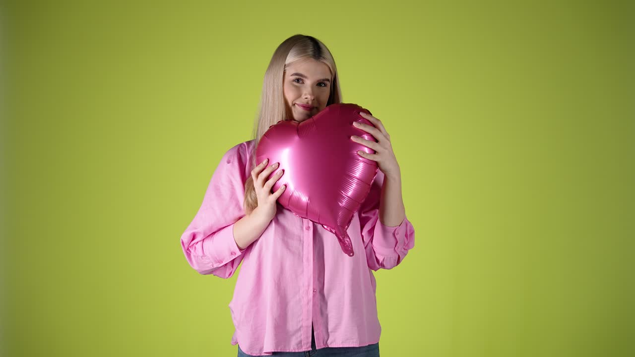 joven mujer rubia caucásica juega con un globo en forma de hogar sonriendo, estudio