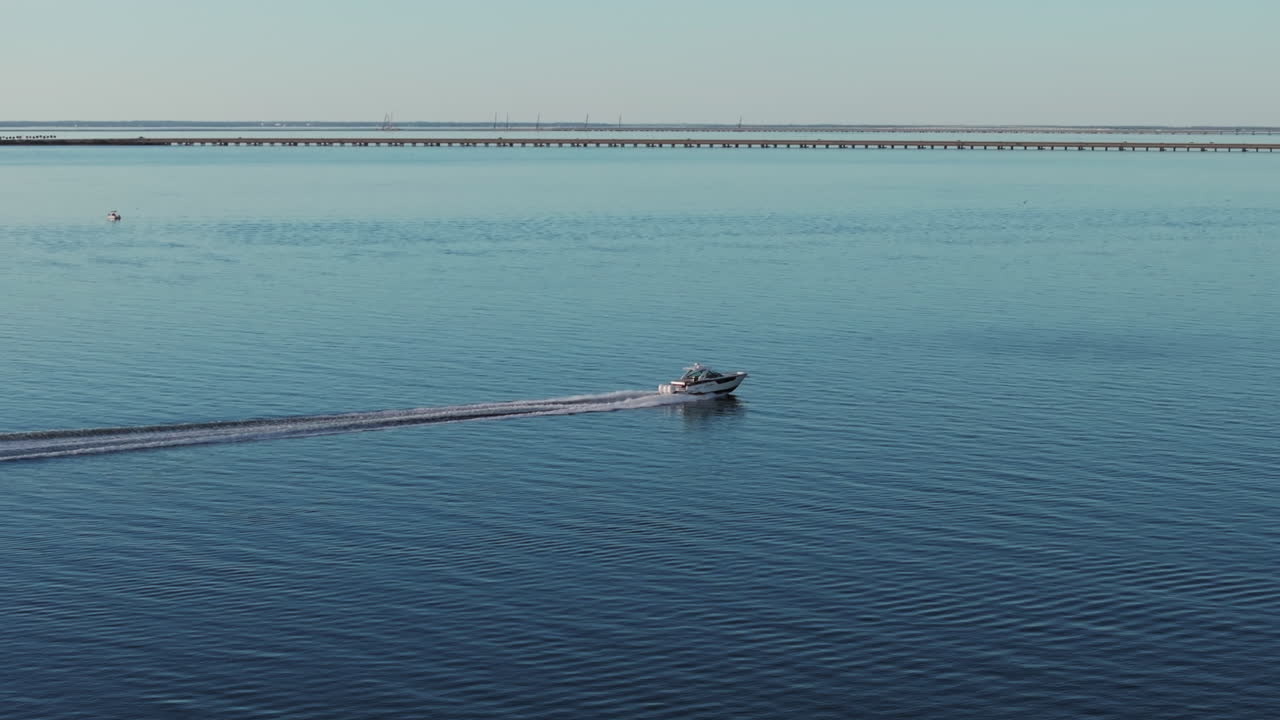 High-speed motorboat cruising across calm blue coastal Florida waters, leaving a foamy wake behind. Scenic view with a long bridge in the background. Perfect for travel, adventure, and marine themes.