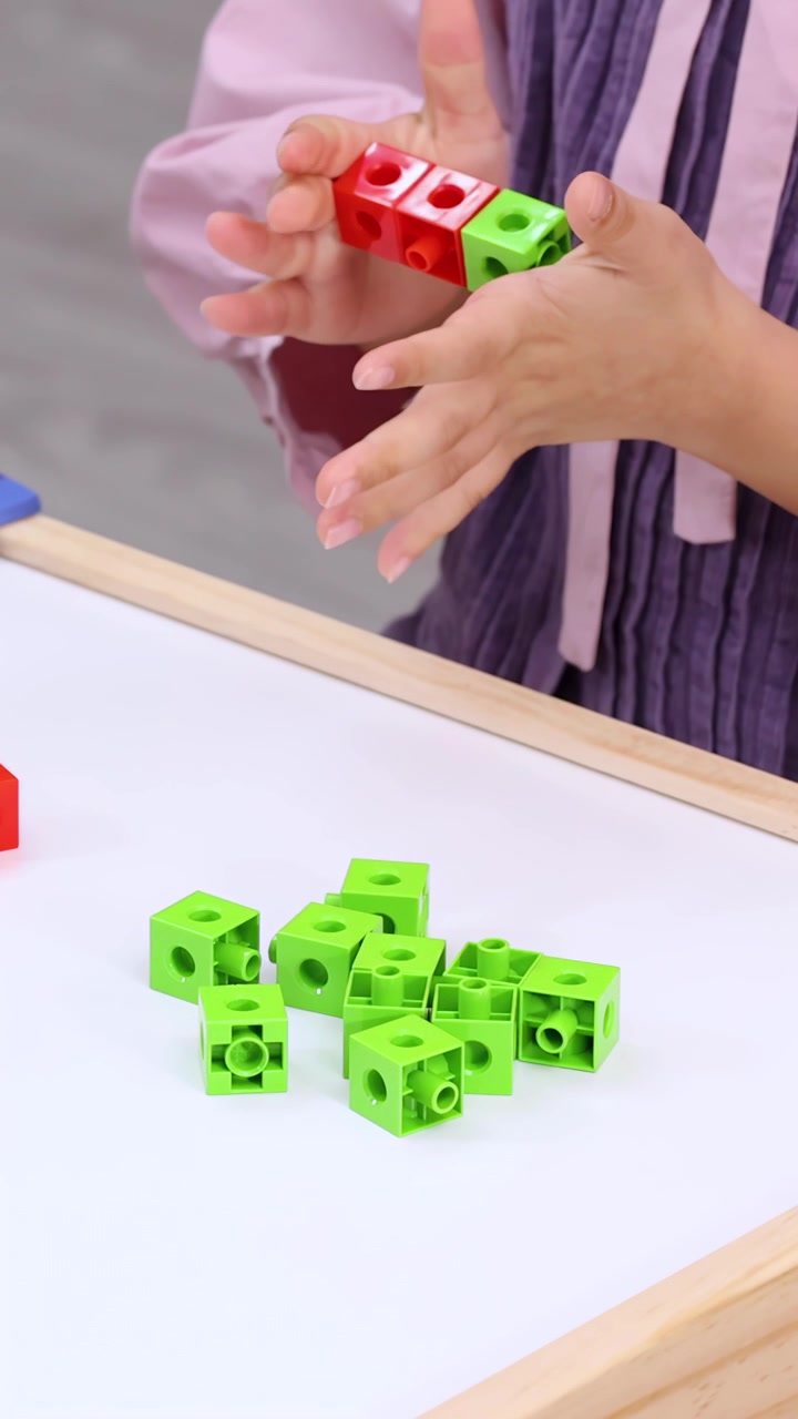 Child’s hands connect red and green counting cubes on white tabletop with steady close-up framing