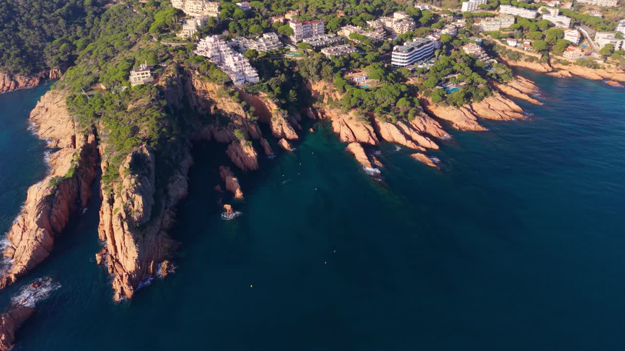 Rekaman rekaman stok drone udara yang terbang di atas garis pantai berbatu Sant Feliu de Guixols yang memukau di Costa Brava, Spanyol, menampilkan vila-vila putih mewah yang terletak di antara pepohonan pinus hijau