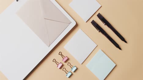 overhead view of notebook, pens and stationery arranged on beige background, in slow motion