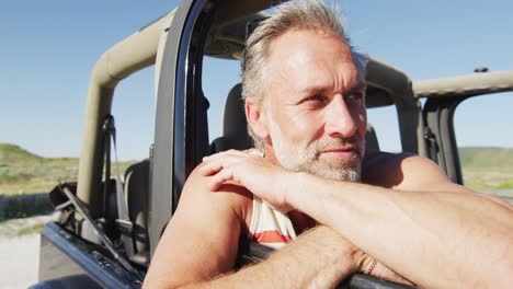 feliz hombre caucásico sentado en el coche disfrutando de la vista en un día soleado en la playa