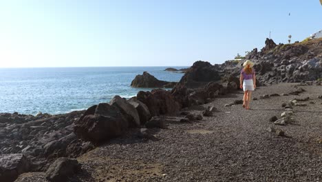 young woman walking alongside of tenerife coastline, back view