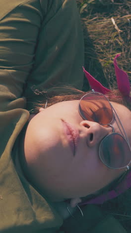 tired overweight girl tourist with sunglasses rests on dry grass at campsite in calm autumn evening close view
