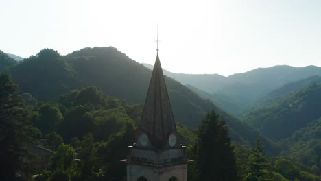 aerial dolly around top of parish church located in forested hillside at arola, italy