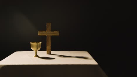 religious concept shot with wooden cross and chalice on altar in pool of light