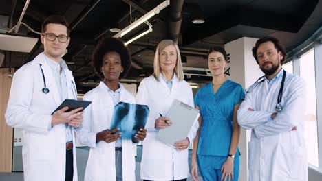 equipo de médicos multiétnicos con batas blancas mirando la cámara de buen humor mientras sostienen una radiografía y una tableta en un hospital moderno