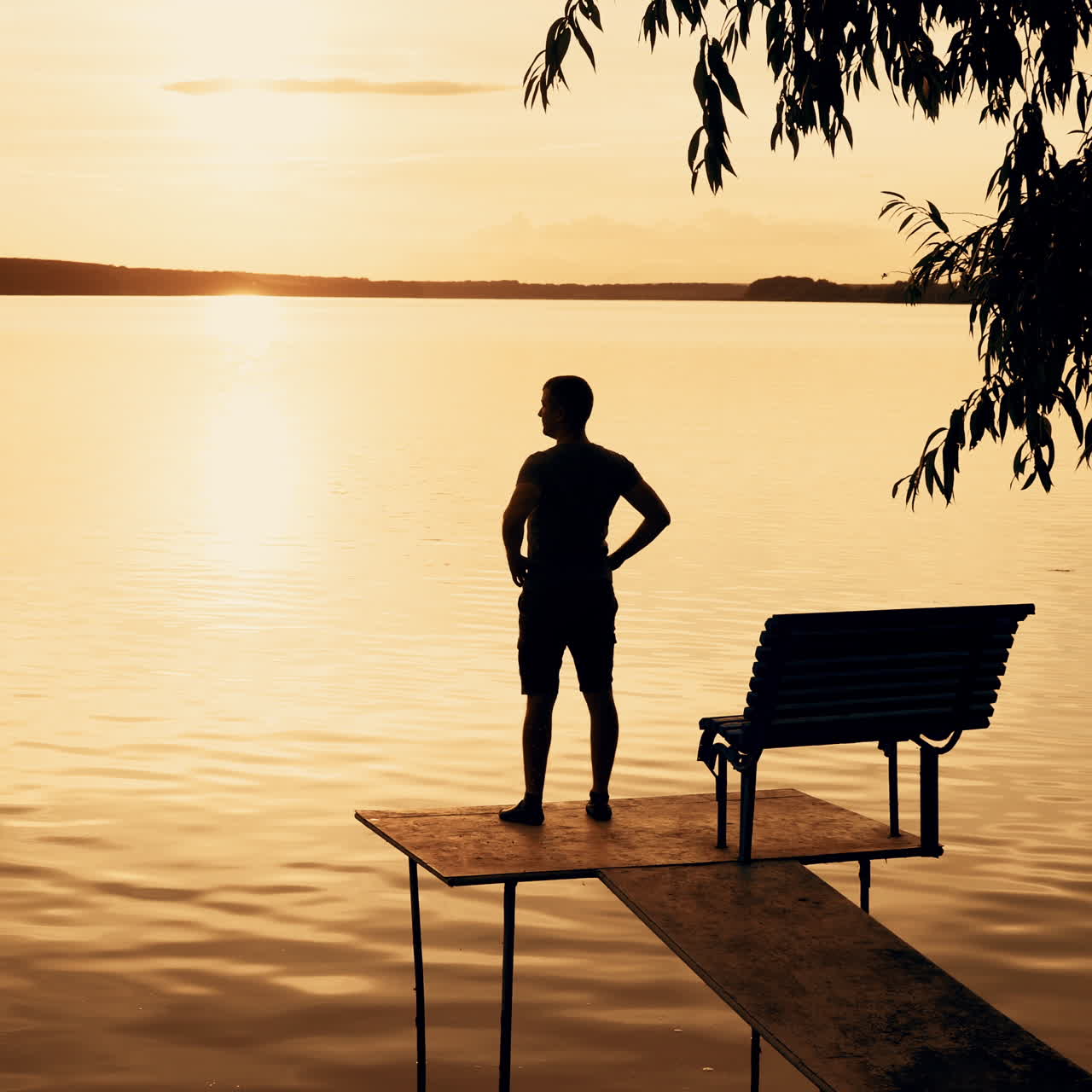 A young man goes to the bridge on the river and looks on a beautiful view of the sunset. Orange background.