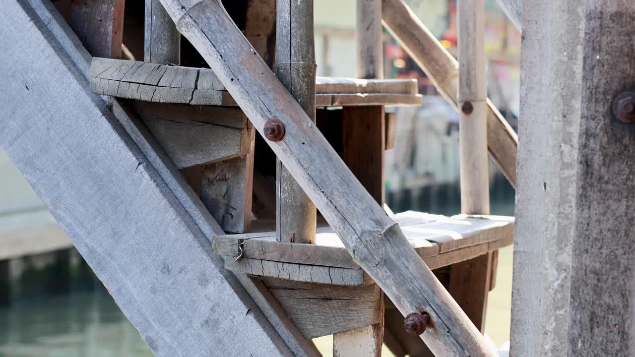 Close-up view of wooden stairs at Khlong Lat Mayom Floating Market, Bangkok. Natural lighting highlights the rustic texture and water reflections