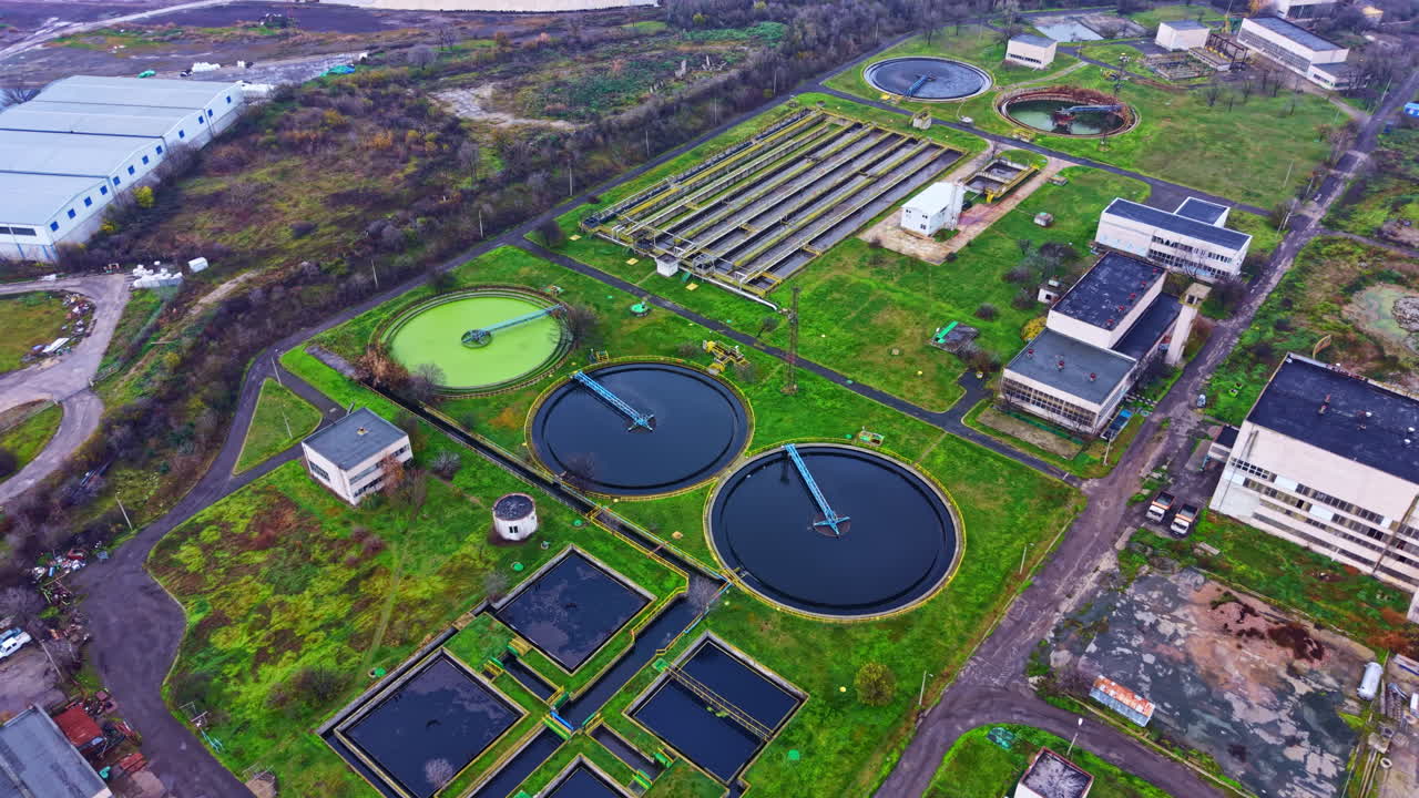 Water treatment facility with several large tanks and green areas in a industrial location during daylight hours in an urban area