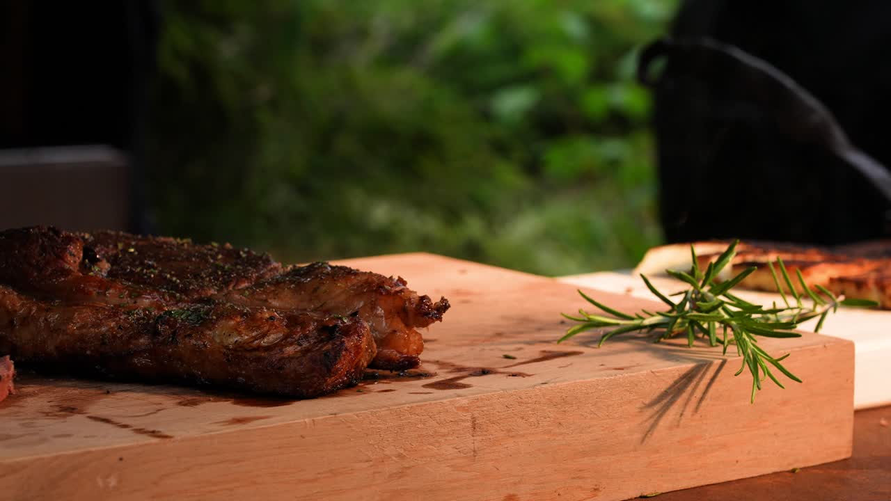 Close-up of a juicy grilled steak being carefully sliced with a sharp knife in an outdoor kitchen. Fresh rosemary adds a natural aroma and highlights the rustic outdoor cooking atmosphere