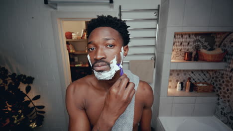 young african american man shaving his face in bathroom