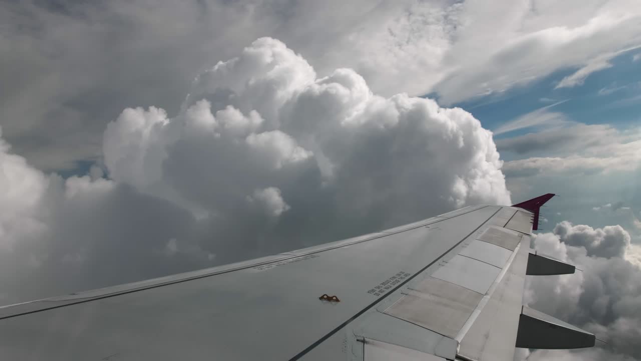 기체와 부피의 회색 구름과 파란 하늘을 지나가는 비행기 비행. 비행기의 조종석에서 1인칭으로 볼 때, 프레임에는 분홍색 날개 끝 장치가 있는 회색 날개가 있습니다.